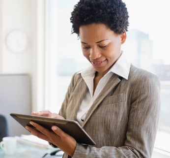 Un hombre de barba con chaqueta de traje en negro, gorra negra y audífonos en azul mira un teléfono. Fondo de ciudad borrosa.