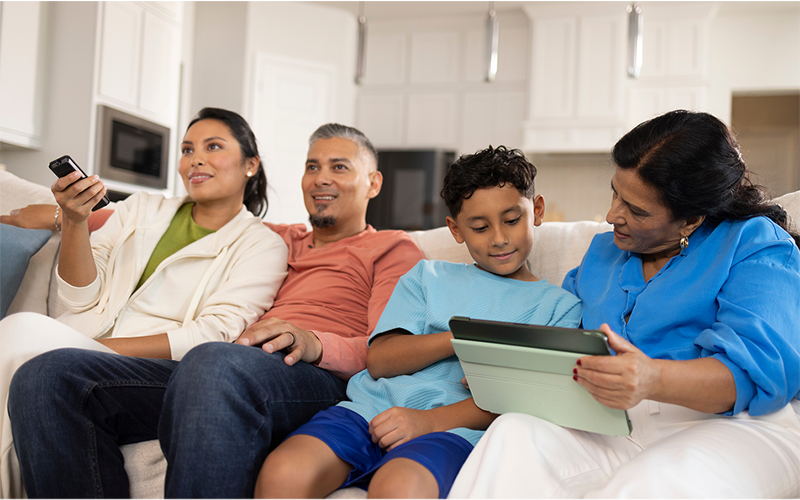A Family is sitting on a couch watching TV and laptop