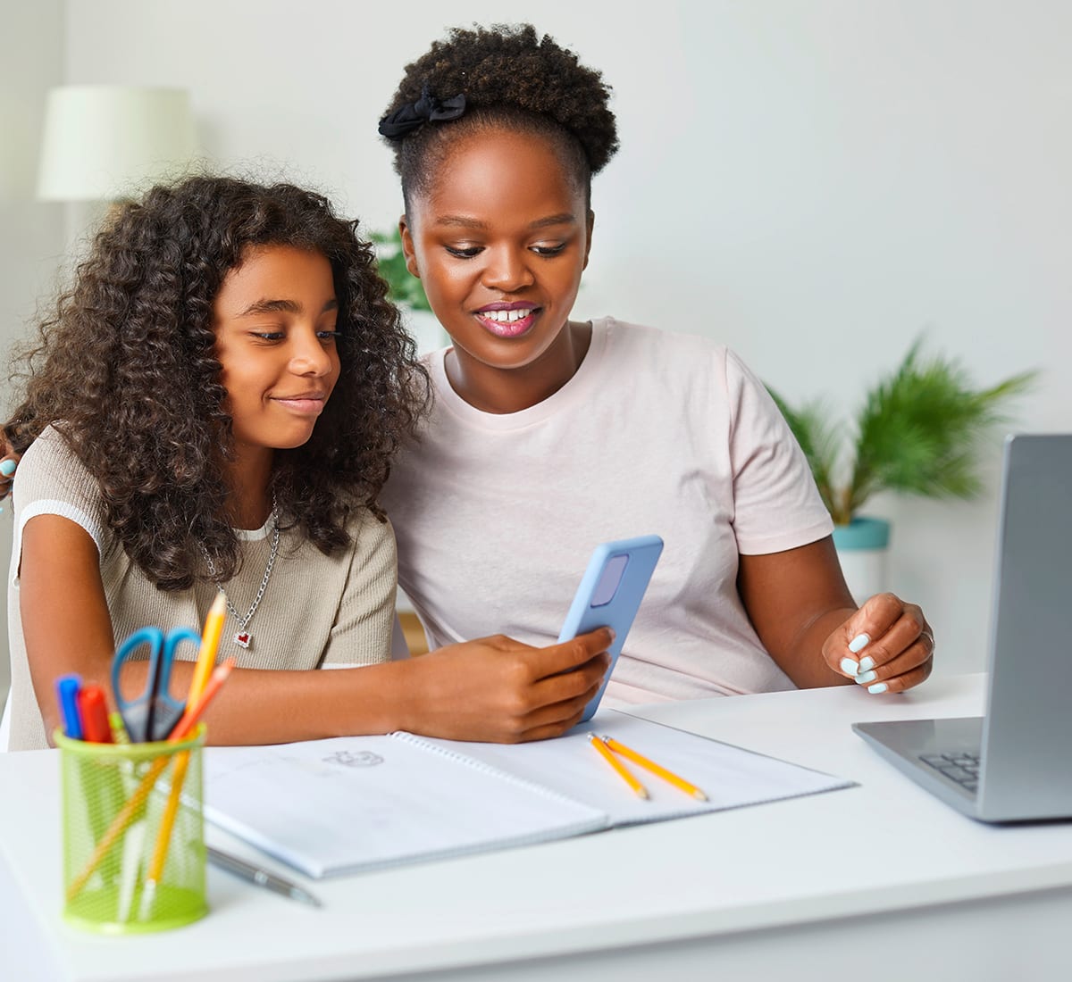 sisters looking at phone while doing homework